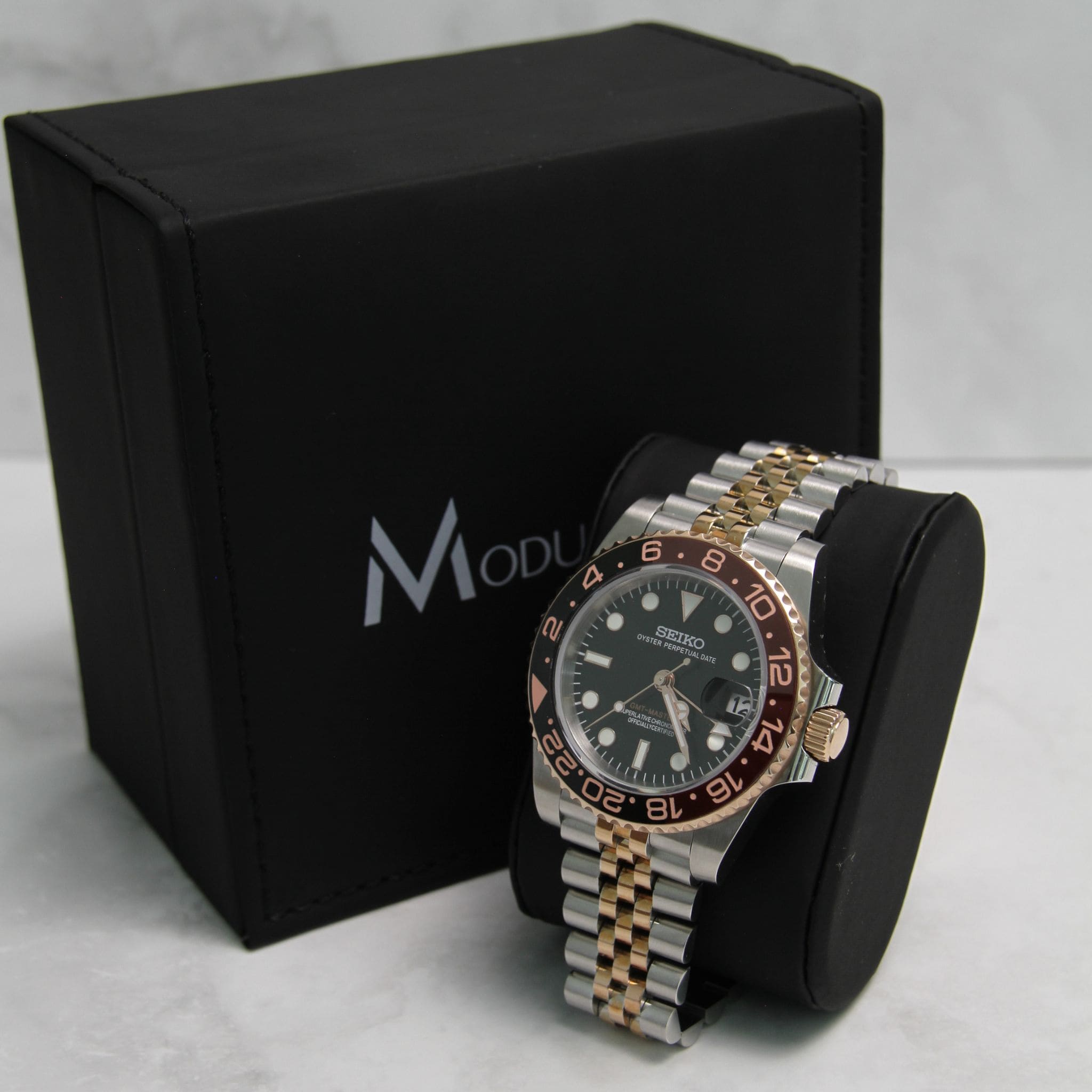 Montre Seiko Mod gmt root beer en gros plan sur coussin noir avec écrin en arrière plan.
