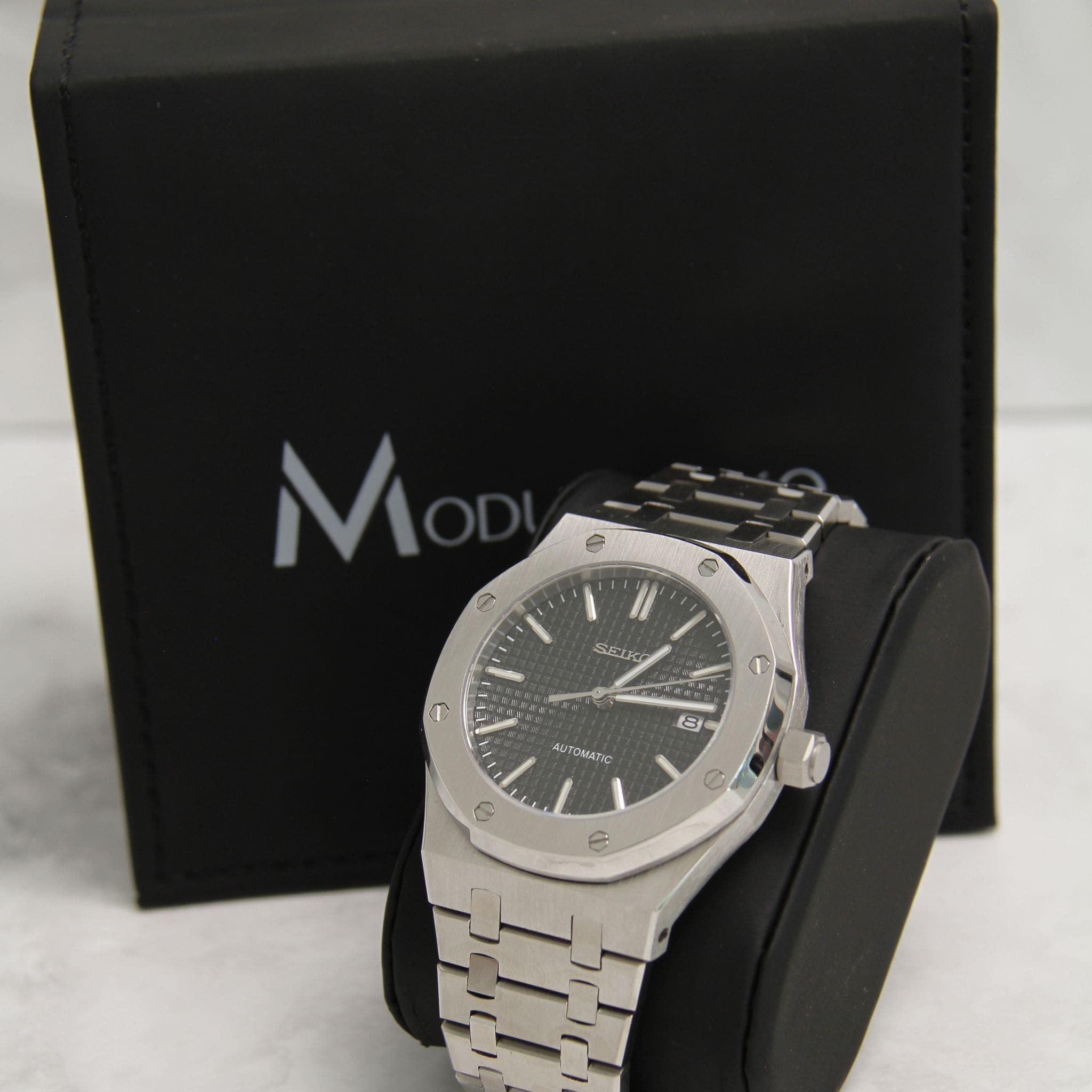 Montre Seiko Mod Royal oak noir sur coussin noir avec écrin en arrière plan
